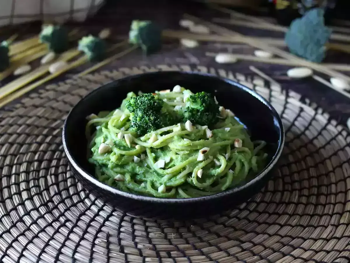 En skål med krämig broccoli pasta, toppad med broccolibuketter och hackade nötter. En härlig och grön måltid.
