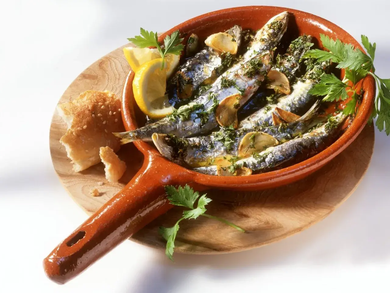 Leckeres Sardinen Rezept in einer Terracotta-Pfanne mit Zitrone, Knoblauch und Petersilie, dazu Brot.