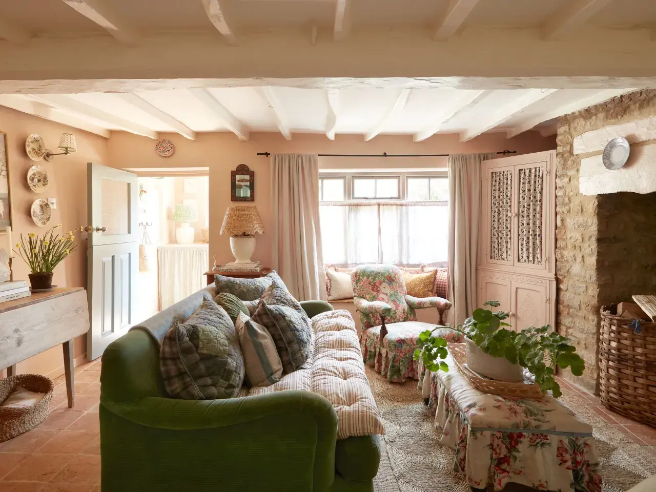 Cozy living room with a green sofa, floral armchair, and charming granny decor. Exposed beams and stone accents add rustic warmth.