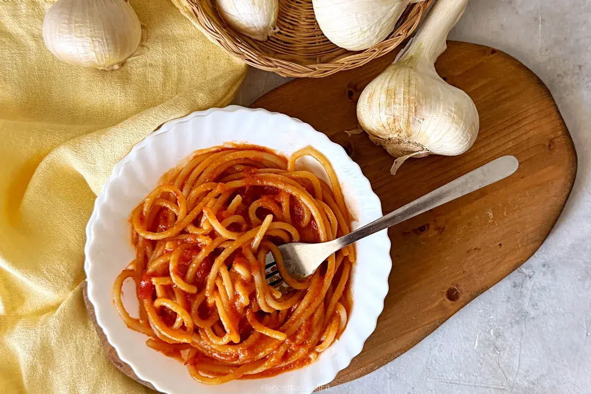 Piatto di pici all'aglione fumanti, con aglio fresco in primo piano. Un classico della cucina toscana.