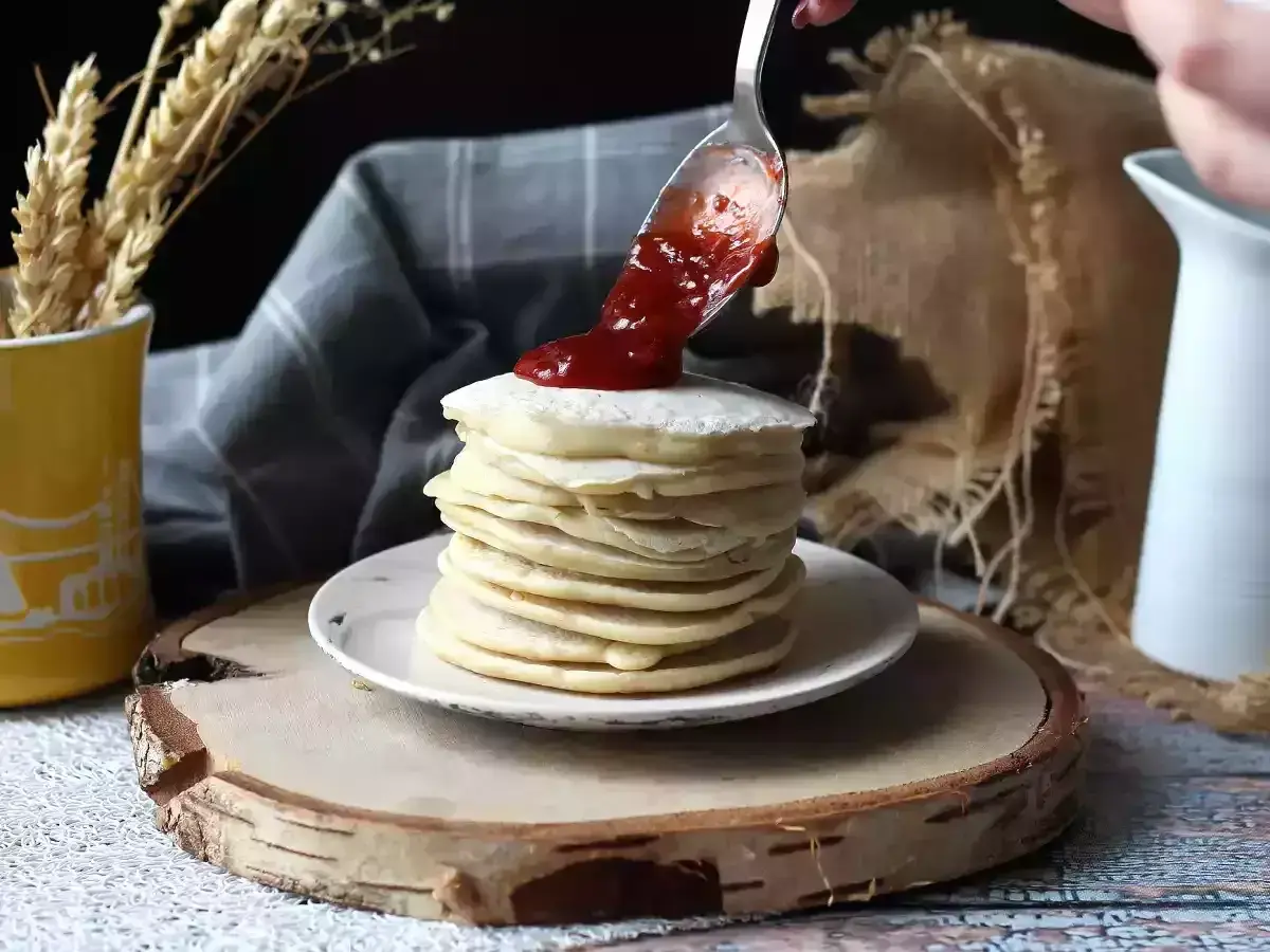 Una cuchara vierte mermelada sobre una pila de tortitas veganas.