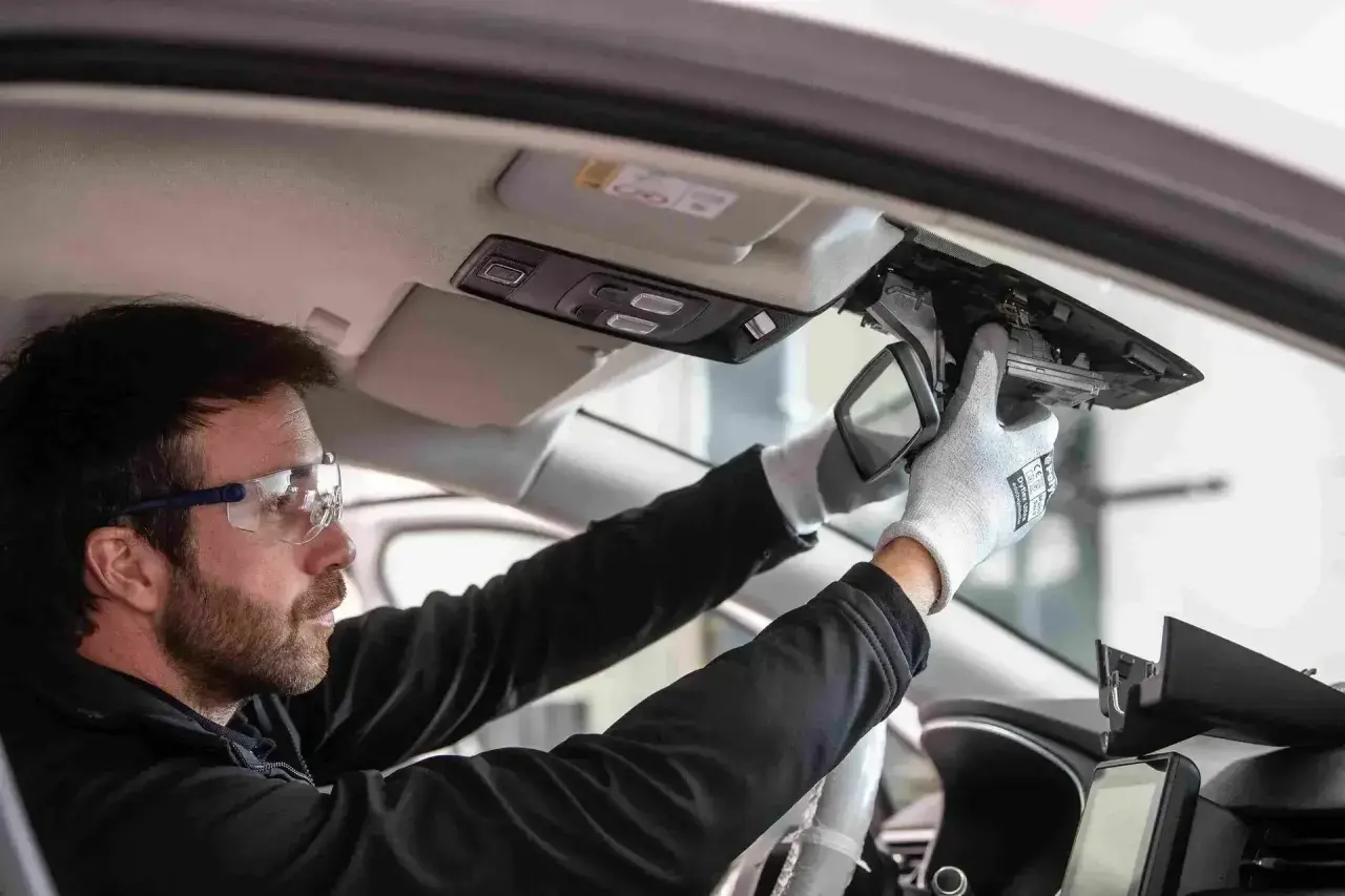 Un technicien porte des lunettes de sécurité et des gants pour démonter le rétroviseur intérieur. C'est le moment pour changer un pare-brise.