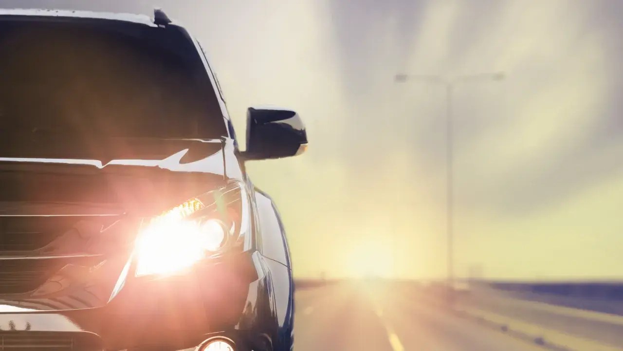 Las luces del coche brillan intensamente al amanecer en una carretera desierta.