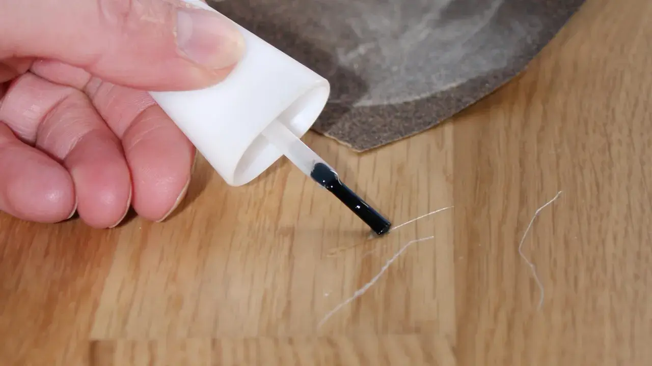 Mit einem Lackstift und Schleifpapier kleine Kratzer auf dem Laminat reparieren.