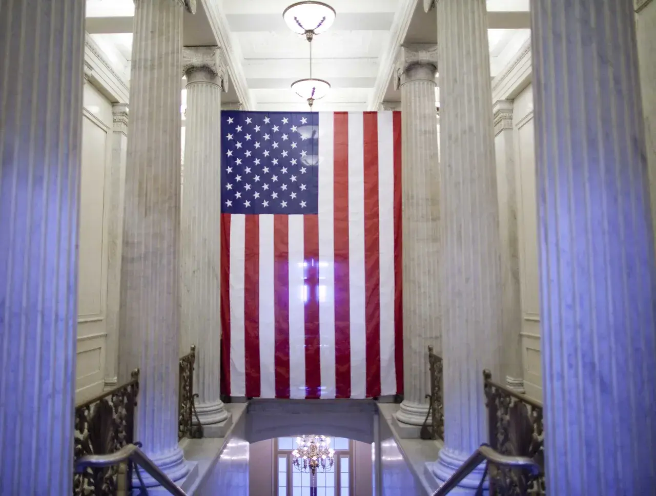 Wielka flaga USA wisi między marmurowymi kolumnami. Czy USA to stany zjednoczone? Tak, to symbol tego kraju.
