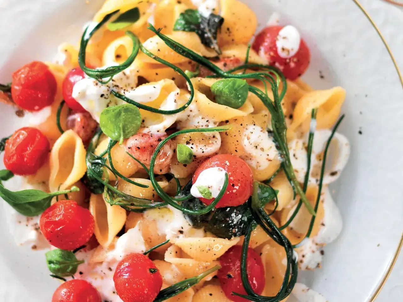 Conchiglie con pomodorini, basilico e una cremosa stracciatella. Un piatto fresco e invitante.