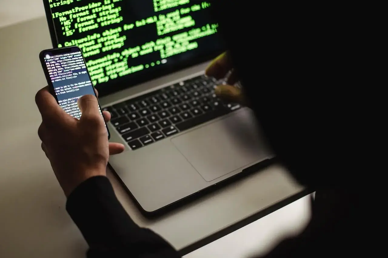 Un développeur web, définition : une personne manipulant du code sur un smartphone et un ordinateur portable, éclairés par la lueur verte des écrans.