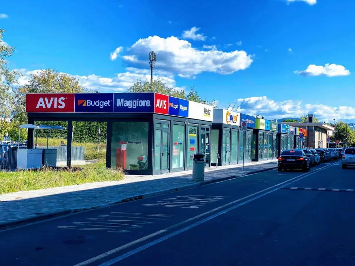 Car rental agencies like Avis, Budget, Maggiore, Hertz, and Europcar line the street, offering options for how to rent a car in Florence, Italy.