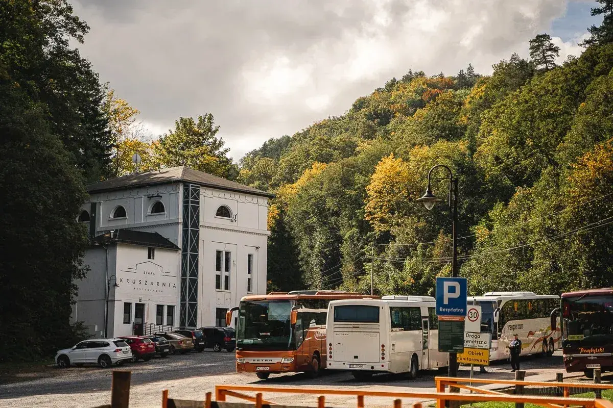 Autobusy czekają przed Starą Kruszarnią w Złotym Stoku. Jesienne drzewa otaczają parking.
