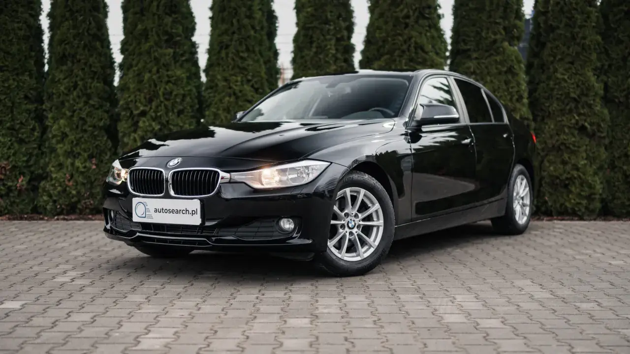 Eleganckie, czarne BMW 318d stoi przed żywopłotem.