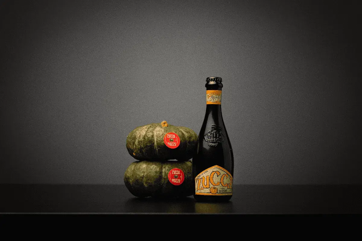 Una bottiglia di birra alla zucca accanto a due zucche impilate.