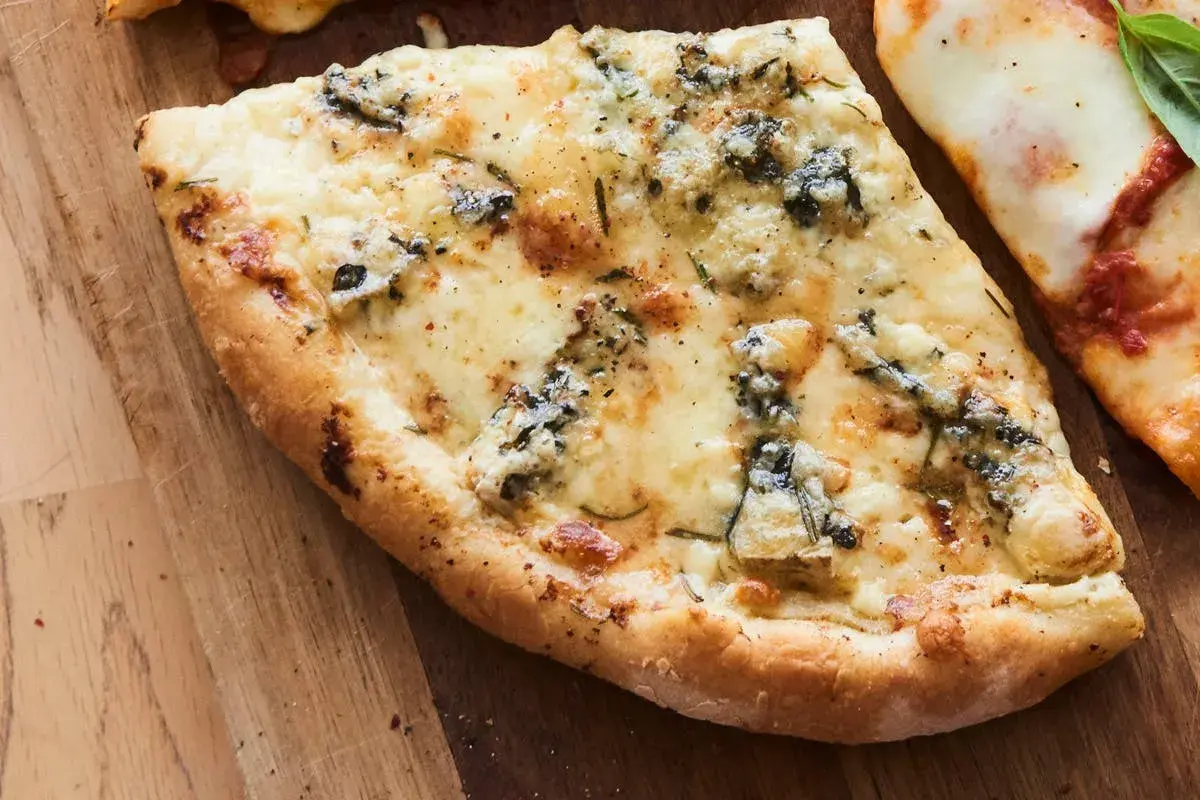 Une part de pizza 4 fromages, avec sa croûte dorée et son mélange de fromages fondus, sur une planche en bois.