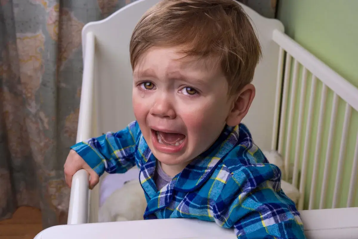 Un niño pequeño con pijama a cuadros llora desconsoladamente en su cuna. Sus ojos están llenos de lágrimas y su boca abierta en un grito.