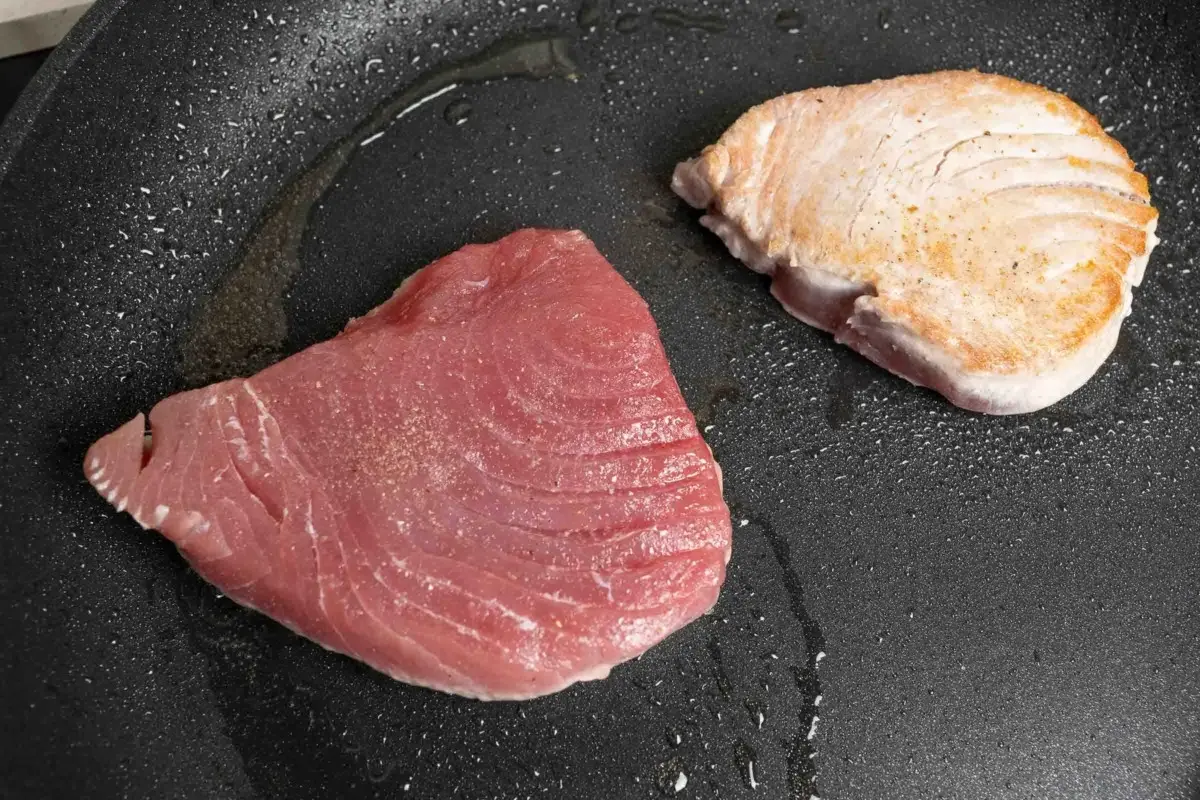 Zwei Thunfischfilets in einer Pfanne: eines roh und rosa, das andere leicht angebraten und goldbraun.