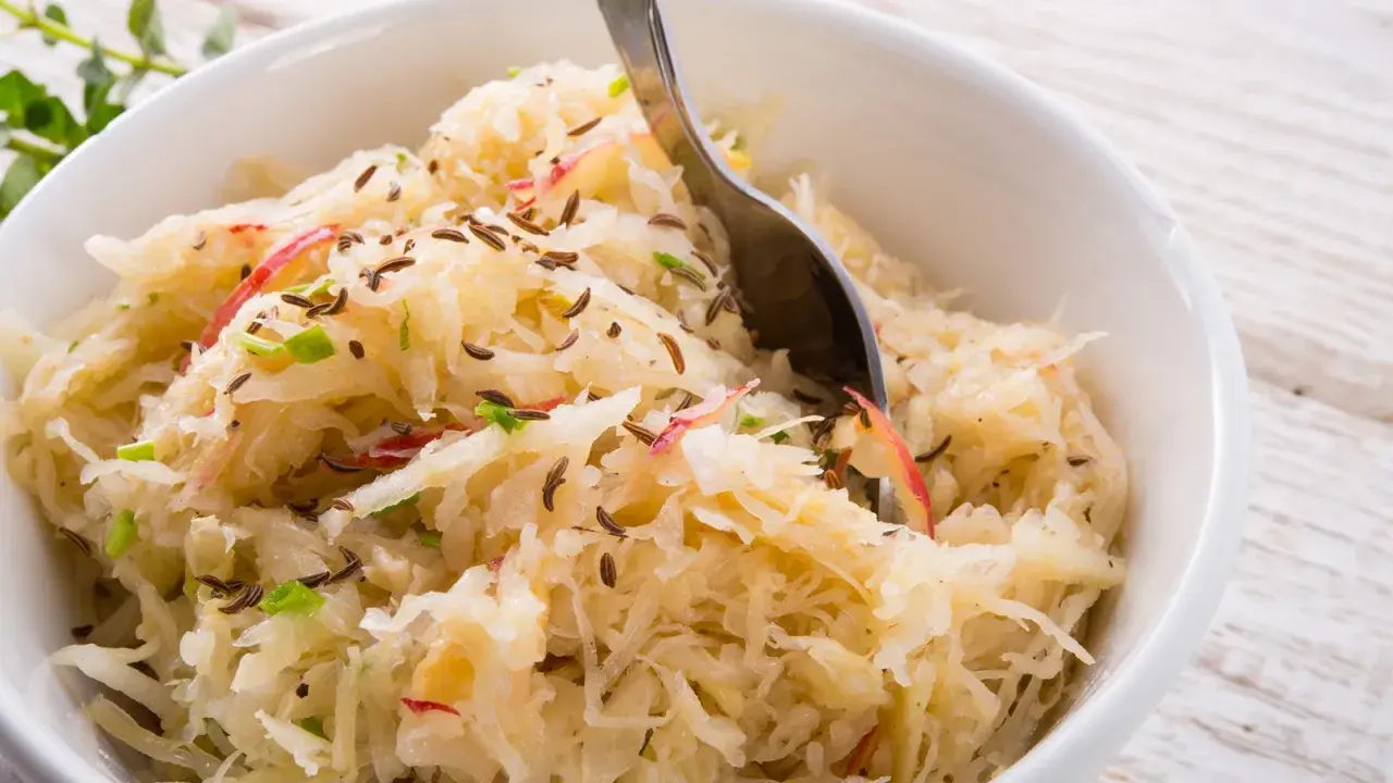 Frisch zubereitetes Sauerkraut mit Kümmel und Apfelstücken in einer weißen Schüssel, bereit zum Servieren.