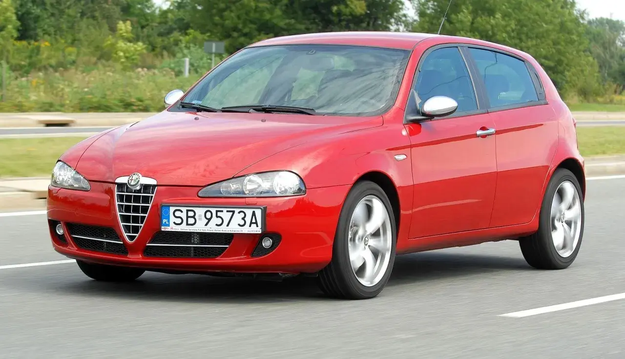 Czerwona Alfa Romeo 147 w ruchu, z widocznymi reflektorami i grillem.