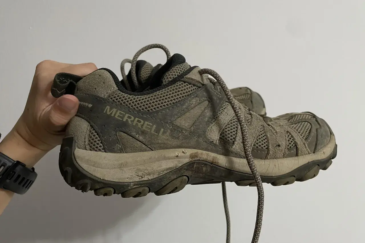 A muddy Merrell hiking shoe is held up, showing its worn tread. This image might inspire ideas on how to rough up the bottom of slippery shoes for better grip.
