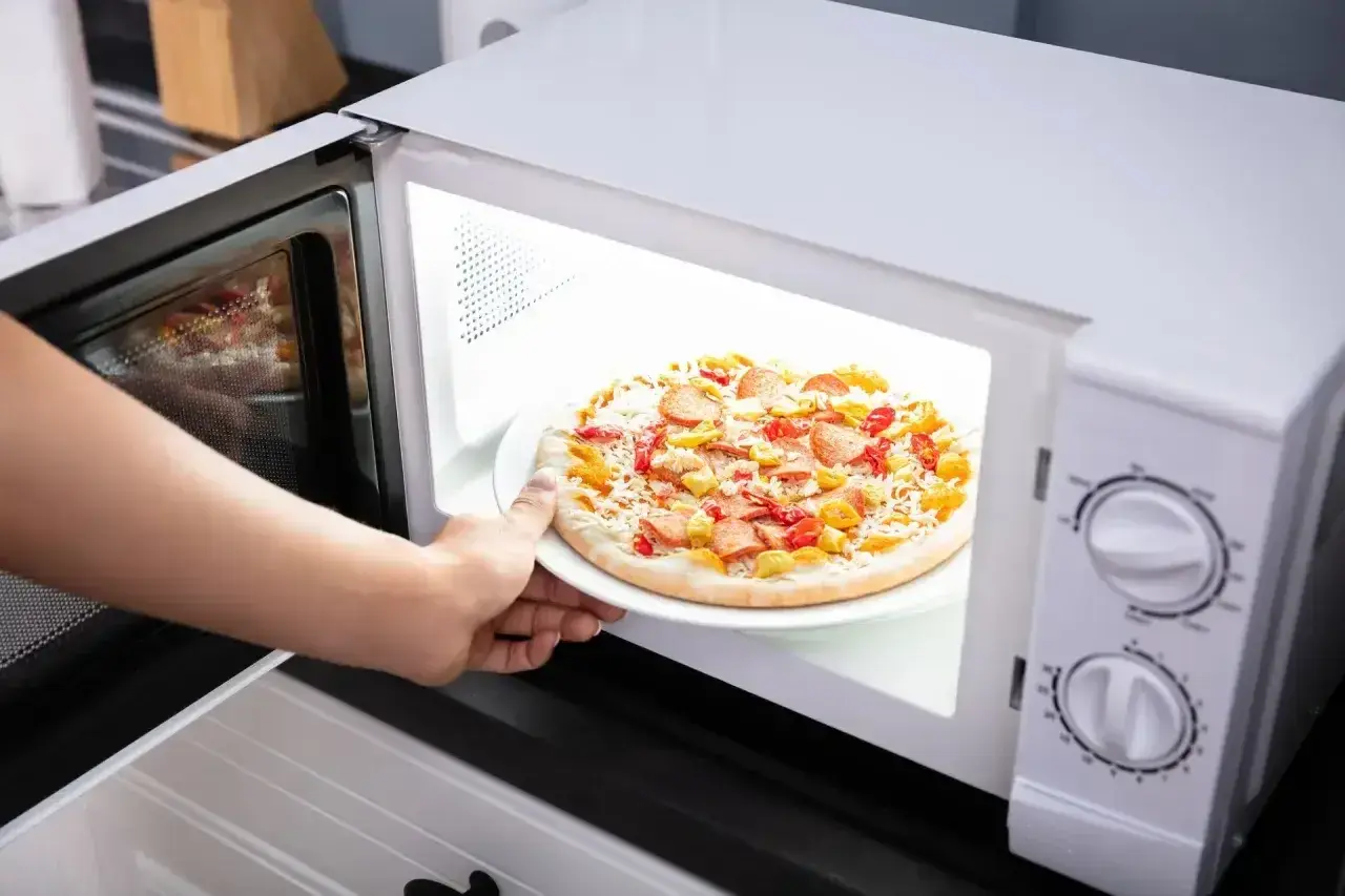 Ręka wkłada mrożoną pizzę do mikrofali. Czy mrożona pizza nadaje się do mikrofali? Zobaczmy!