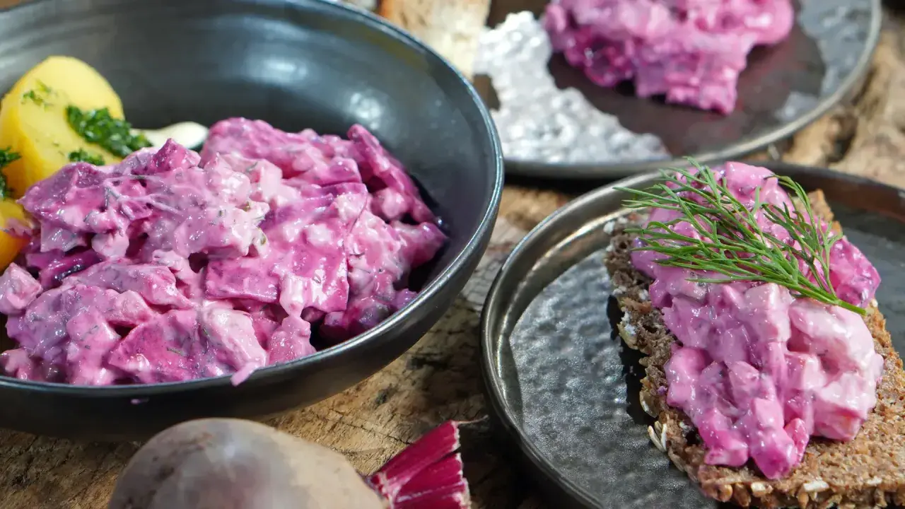 Omas roter Heringssalat, cremig und leuchtend pink, serviert mit Kartoffeln und auf Brot mit Dill.