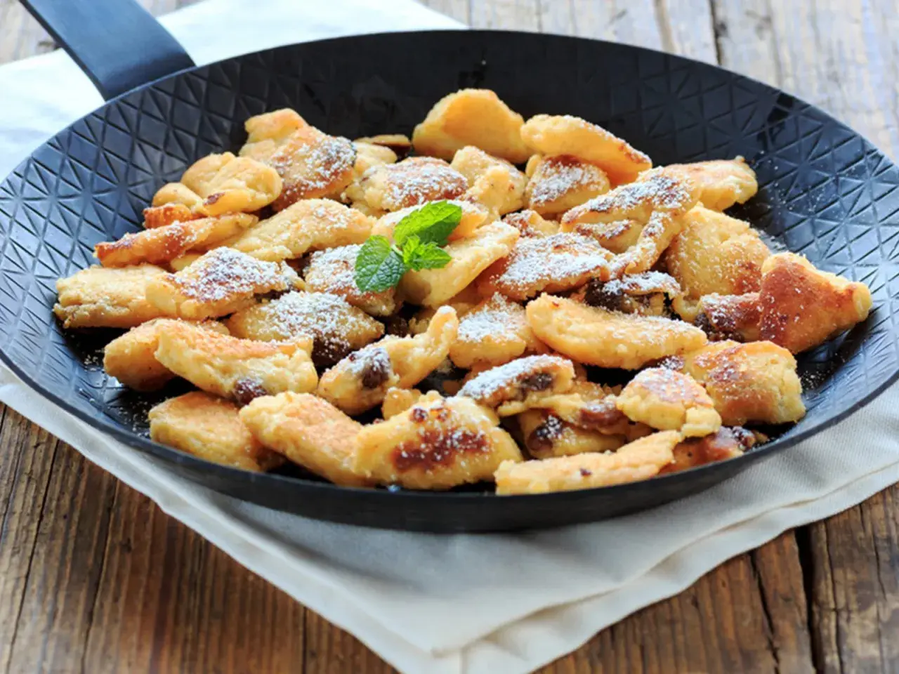 Ein frisch zubereiteter Kaiserschmarrn in Wien, bestäubt mit Puderzucker und garniert mit Minze, serviert in einer Pfanne.