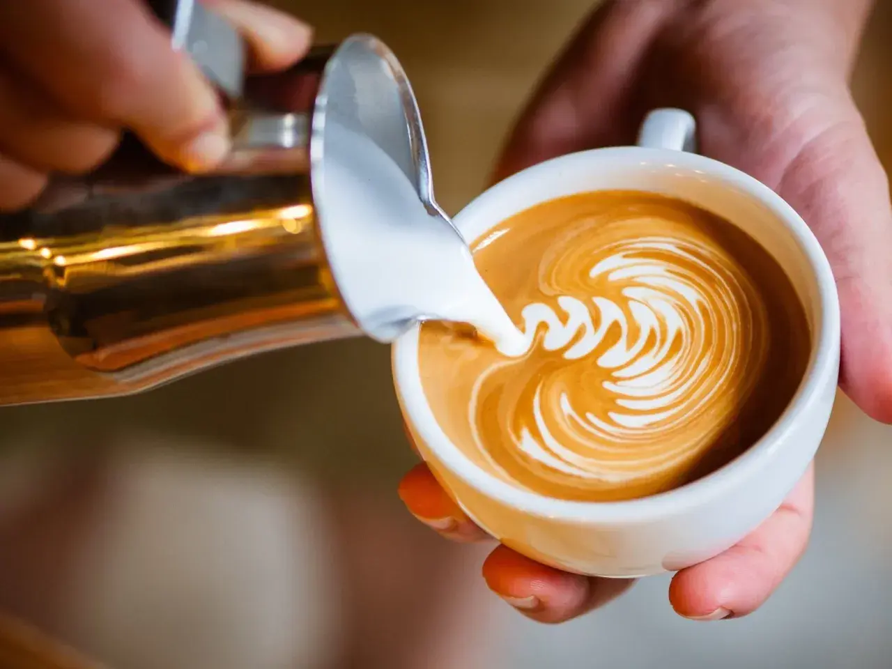 Barista tworzy latte art, wlewając spienione mleko do kawy. Idealne mleko do cappuccino to podstawa pięknego wzoru.
