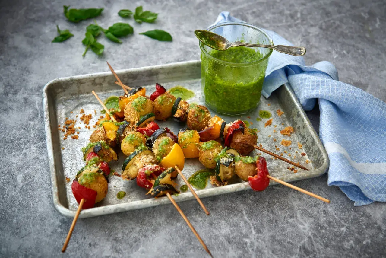 Grillade vegetariska grillspett med potatis, paprika och zucchini, serverade med en grön sås.