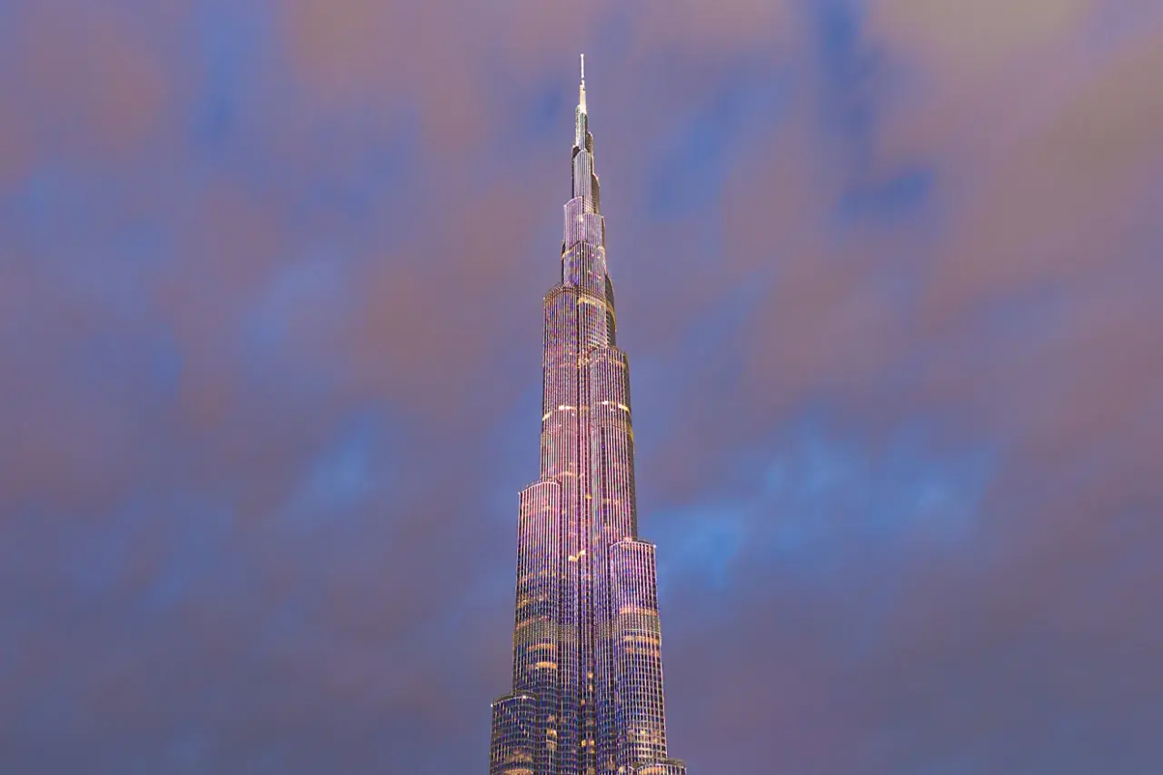 Burj Khalifa oświetlony na fioletowo na tle zachmurzonego nieba.