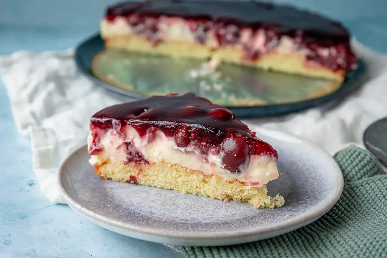 Ein saftiges Stück Kirsch Schmand Kuchen mit Kirschen und einer glänzenden Geleeschicht auf einem Teller.