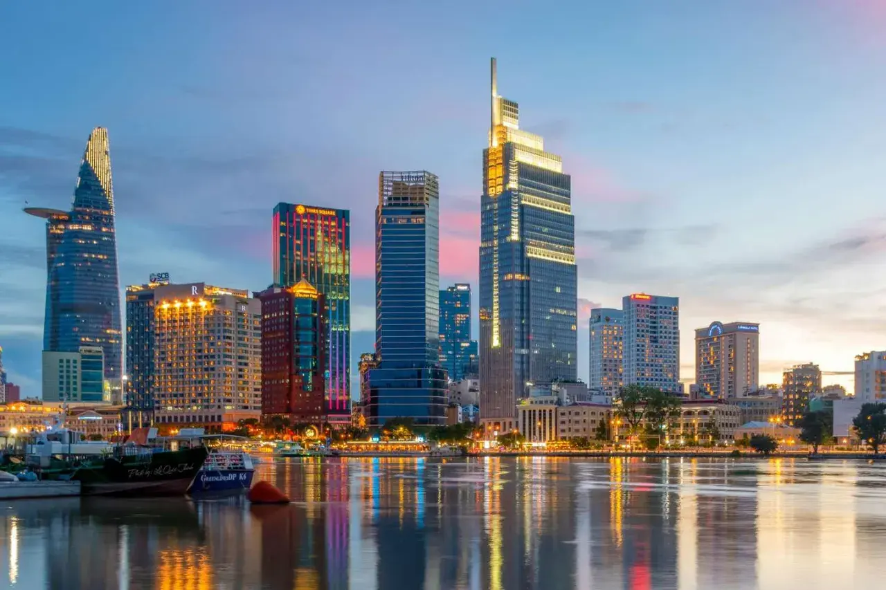 Ho Chi Minh Miasto nocą, z lśniącymi wieżowcami odbijającymi się w wodzie.