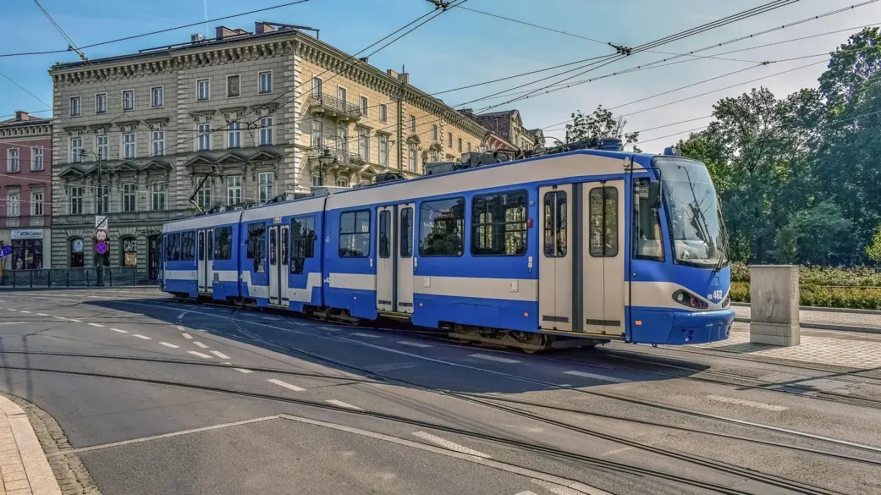 Niebiesko-biały tramwaj na torach w Krakowie. To część krakowskiej komunikacji miejskiej, która przewozi pasażerów przez miasto.