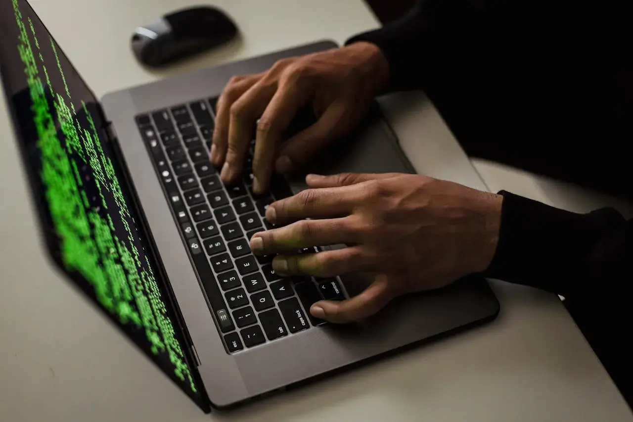 Ręce piszą kod na laptopie, ekran wyświetla zielony tekst. Czy to haker?