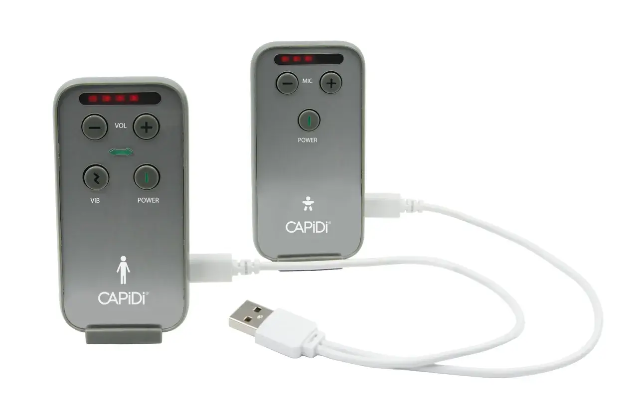 Två grå enheter med texten CAPIDI och knappar för volym, mikrofon, vibration och ström. En vit USB-kabel kopplar ihop dem. En trygghet med capidi babyalarm.