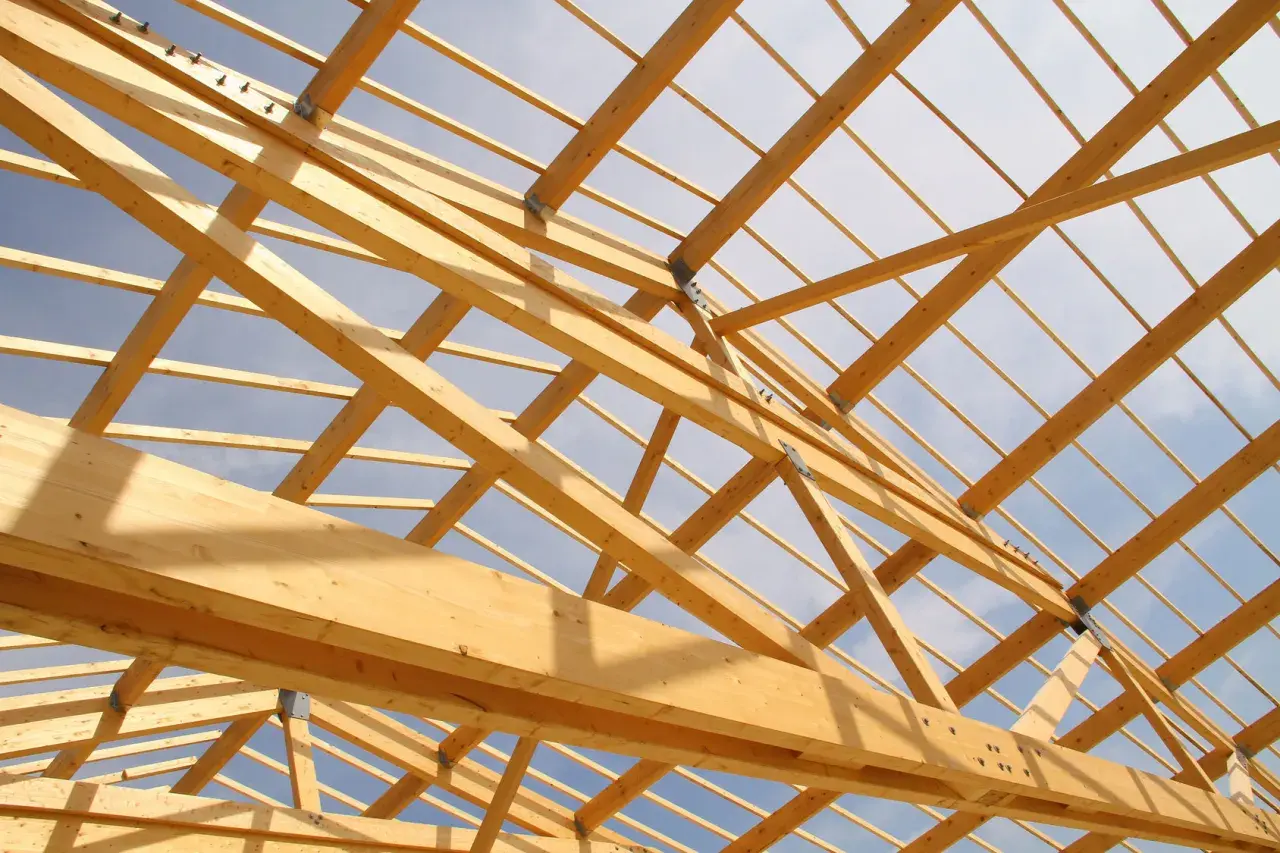 Structure en bois d'une charpente, vue de dessous. Le ciel bleu et nuageux est visible à travers les poutres. Un aperçu pour estimer le prix charpente.