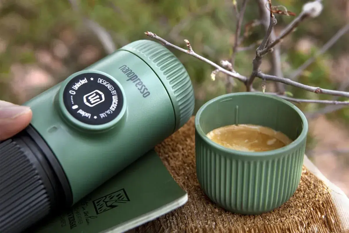 Zielona kawa w górach. Nanopresso i filiżanka świeżego espresso na drewnianym pniu, wśród gałązek. Idealny poranek w naturze.