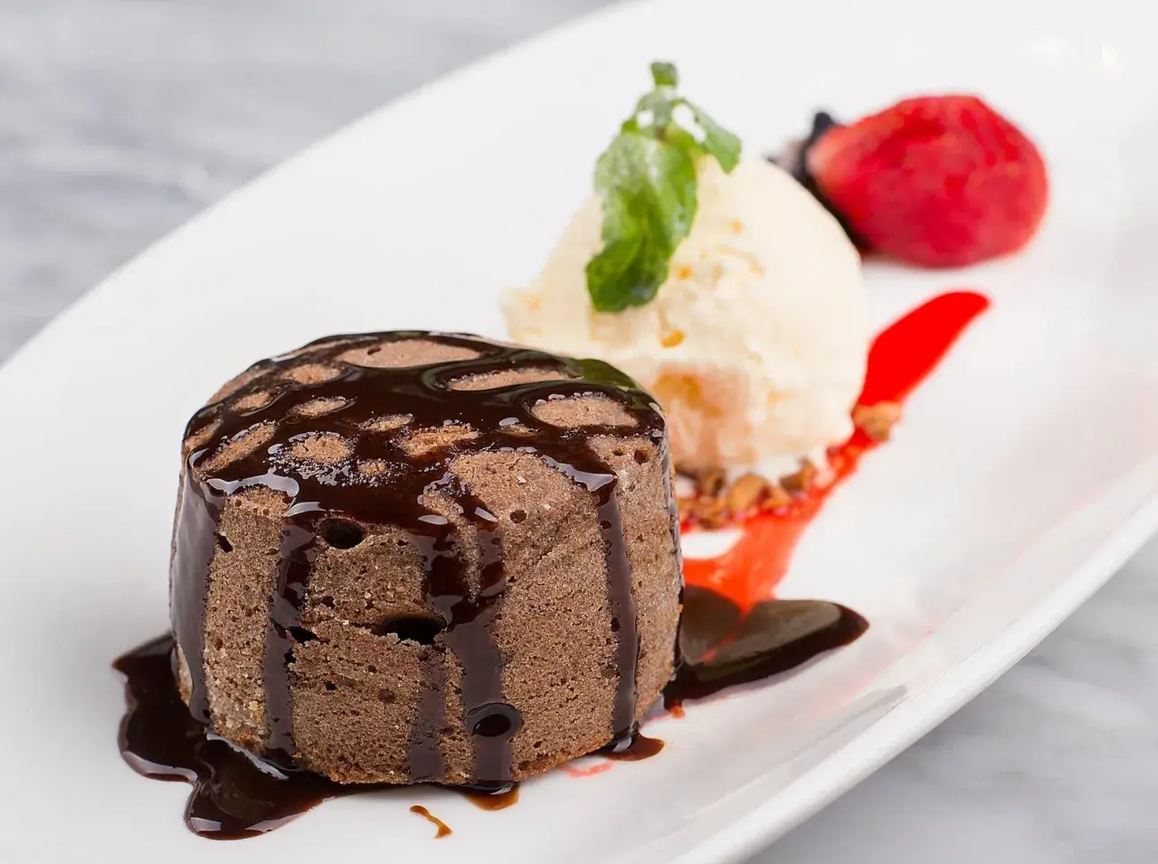 Un fondant au chocolat cœur coulant, servi avec une boule de glace à la vanille, une fraise et un coulis de fruits rouges.