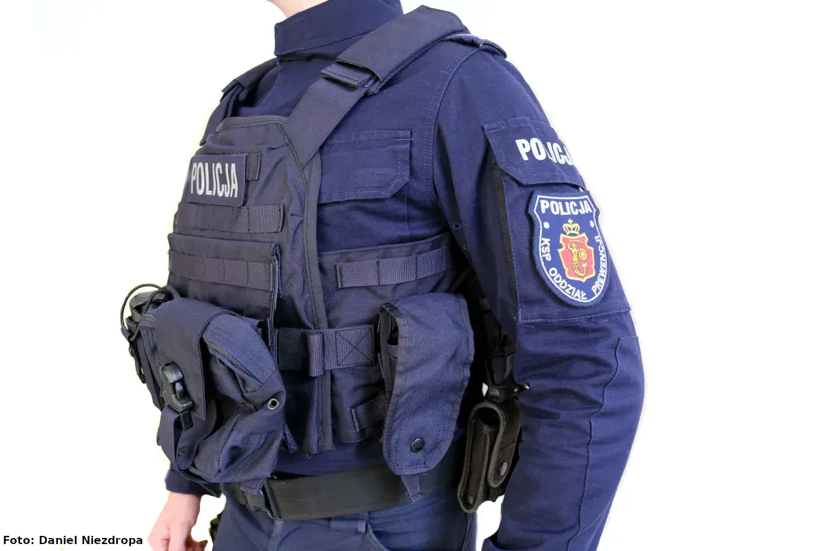 Policjant w pełnym rynsztunku, z kamizelką kuloodporną z napisem "POLICJA" i naszywką "KSP ODDZIAŁ PREWENCJI".