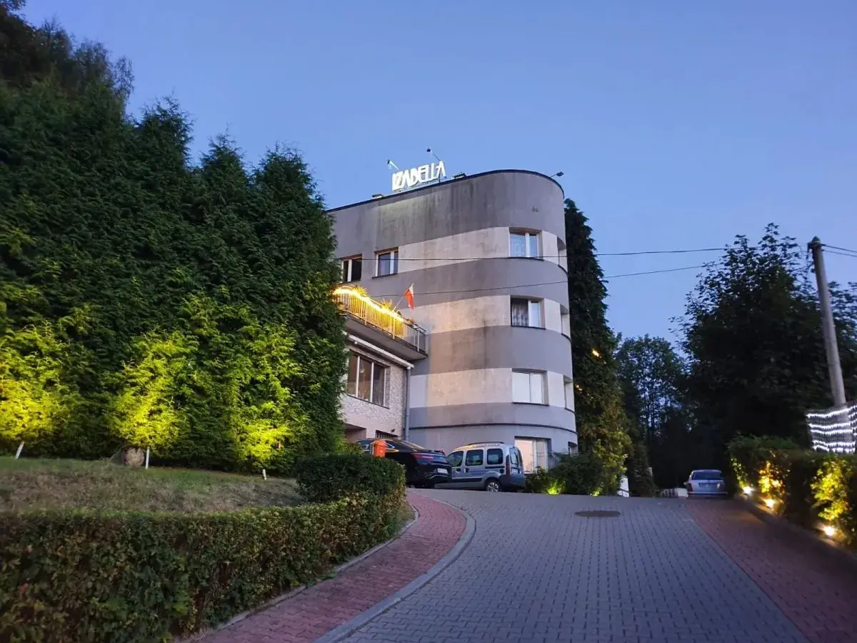 Elegancki hotel Izabella w Puławach, otoczony zielenią i oświetlony wieczorem. Zaprasza do odpoczynku.