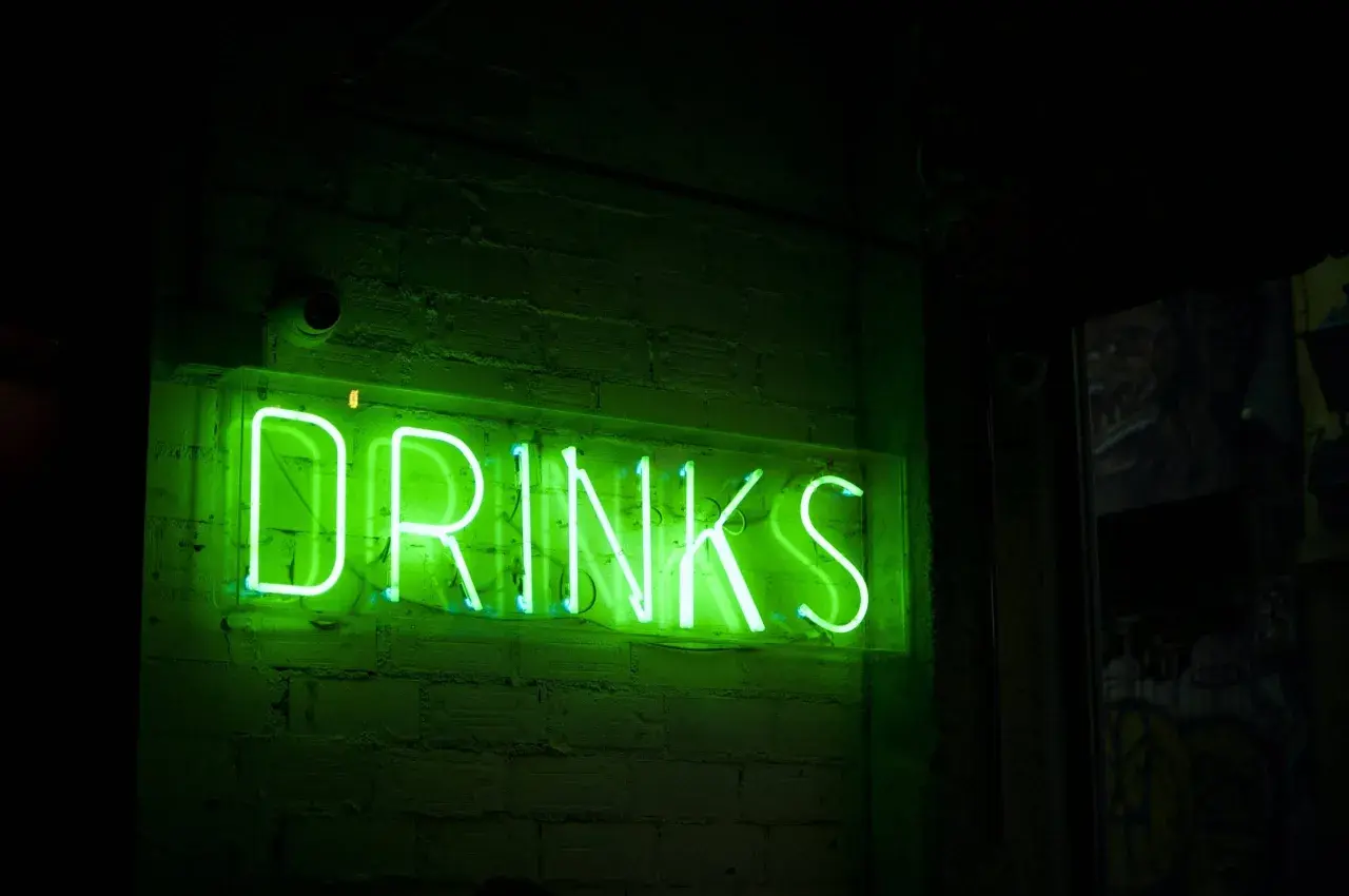 Zielony neon "DRINKS" na ceglanej ścianie. Czas na drinka, jakim alkoholem jesteś?