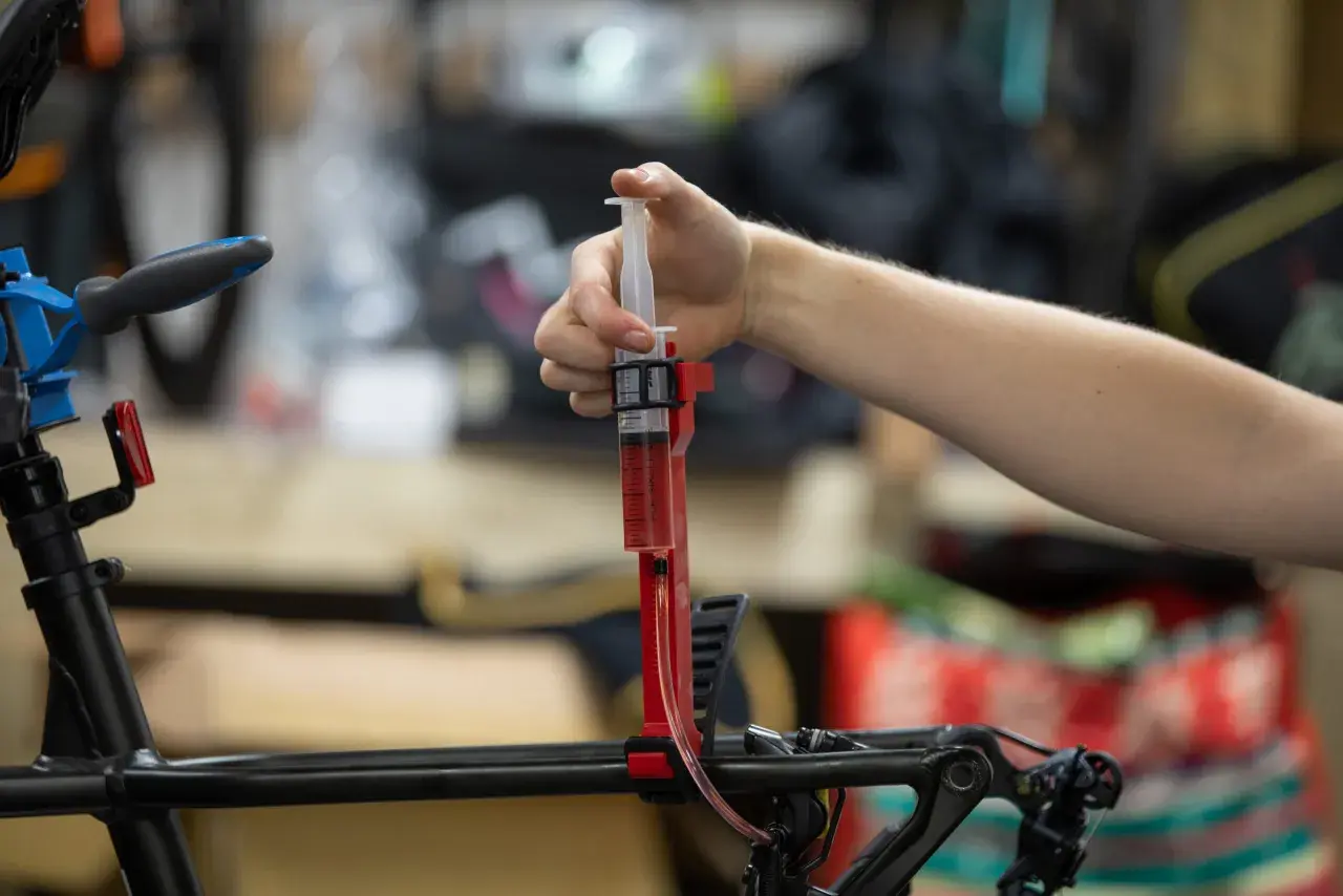 A hand uses a syringe filled with red fluid to bleed bicycle brakes. It's not as hard as you might think!