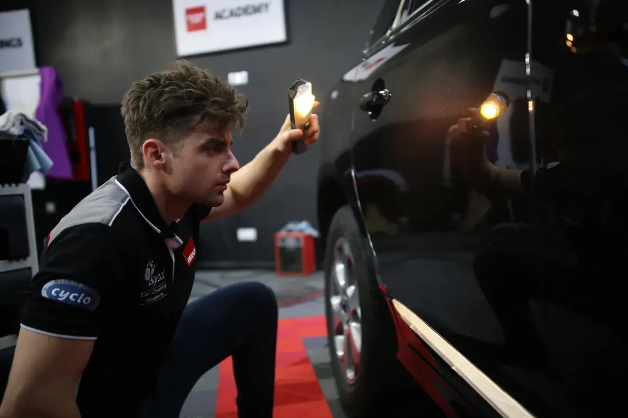 Detailer używa lampy, by ocenić stan lakieru. Widać drobne niedoskonałości na czarnym samochodzie.