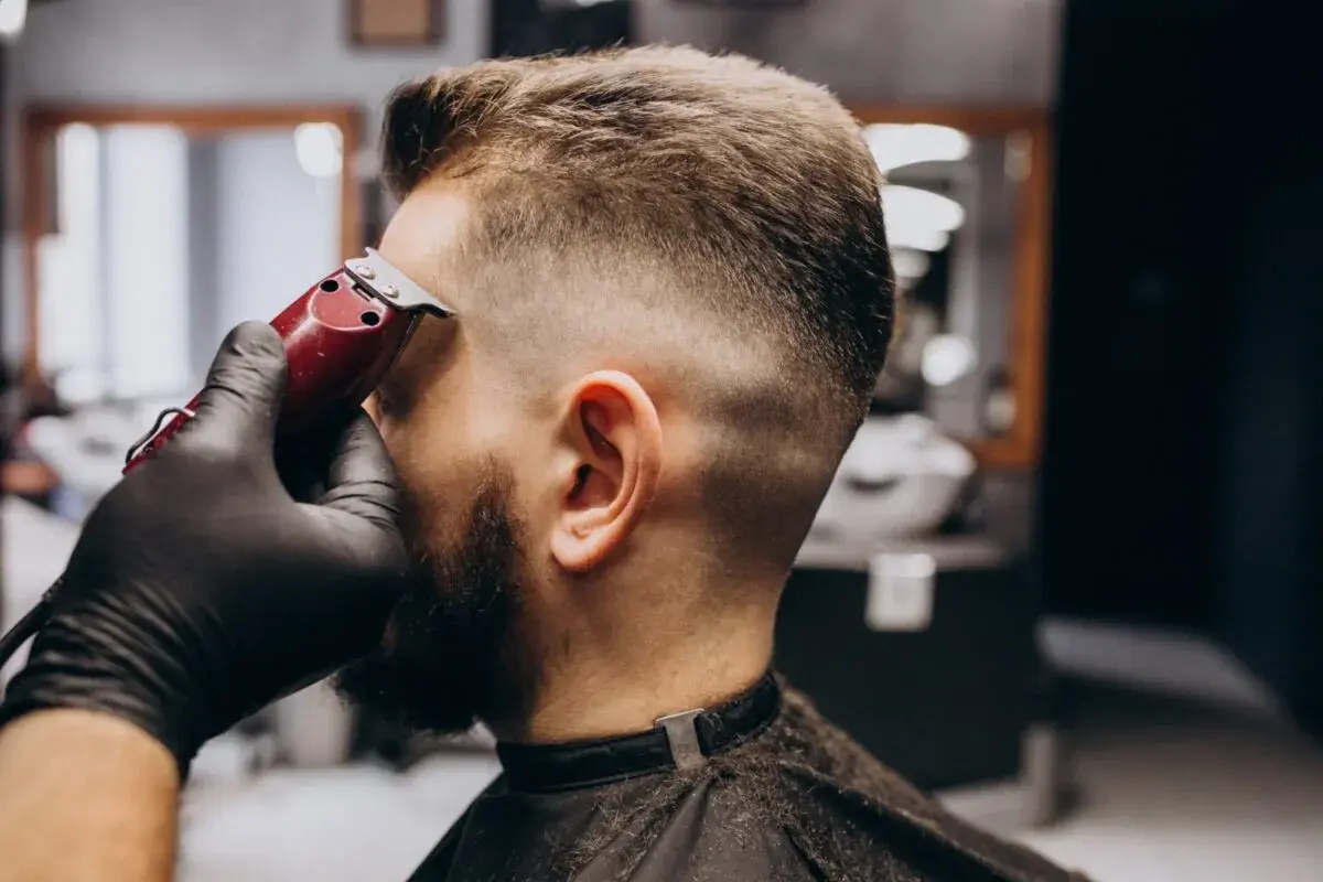 Barbero dando forma a un corte buzz cut fade con máquina. El cabello se desvanece suavemente de corto a largo.