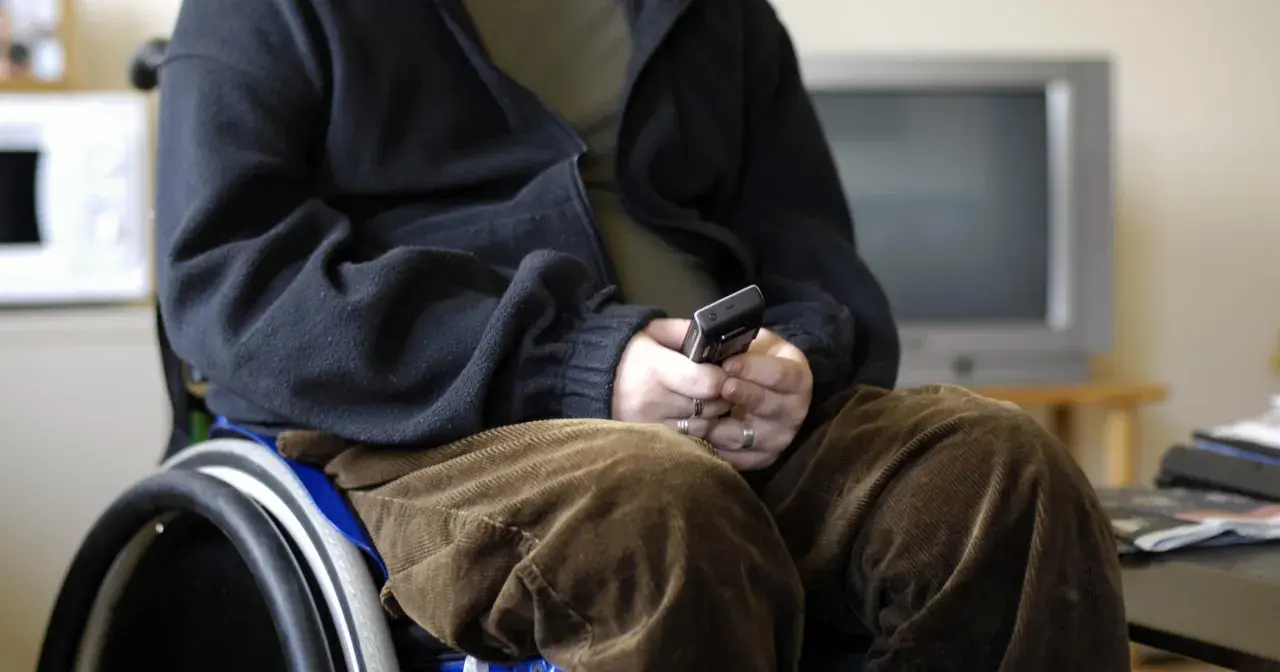 Osoba na wózku inwalidzkim, zmagająca się z atrofia mięśni, trzyma telefon.
