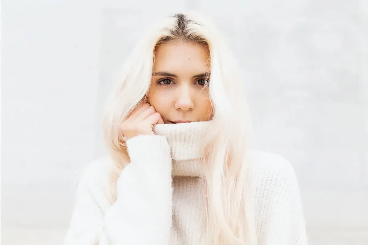 Blondynka w białym golfie, z włosami opadającymi na ramiona, wygląda jak uosobienie stylu vanilla girl.