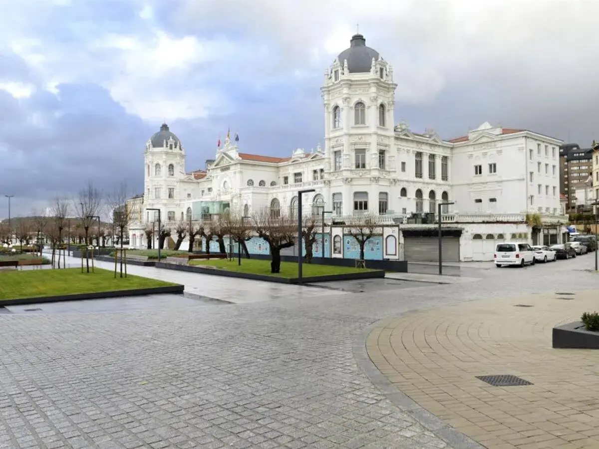 Edificio blanco con cúpulas en la plaza Italia Santander. Árboles desnudos y césped verde.