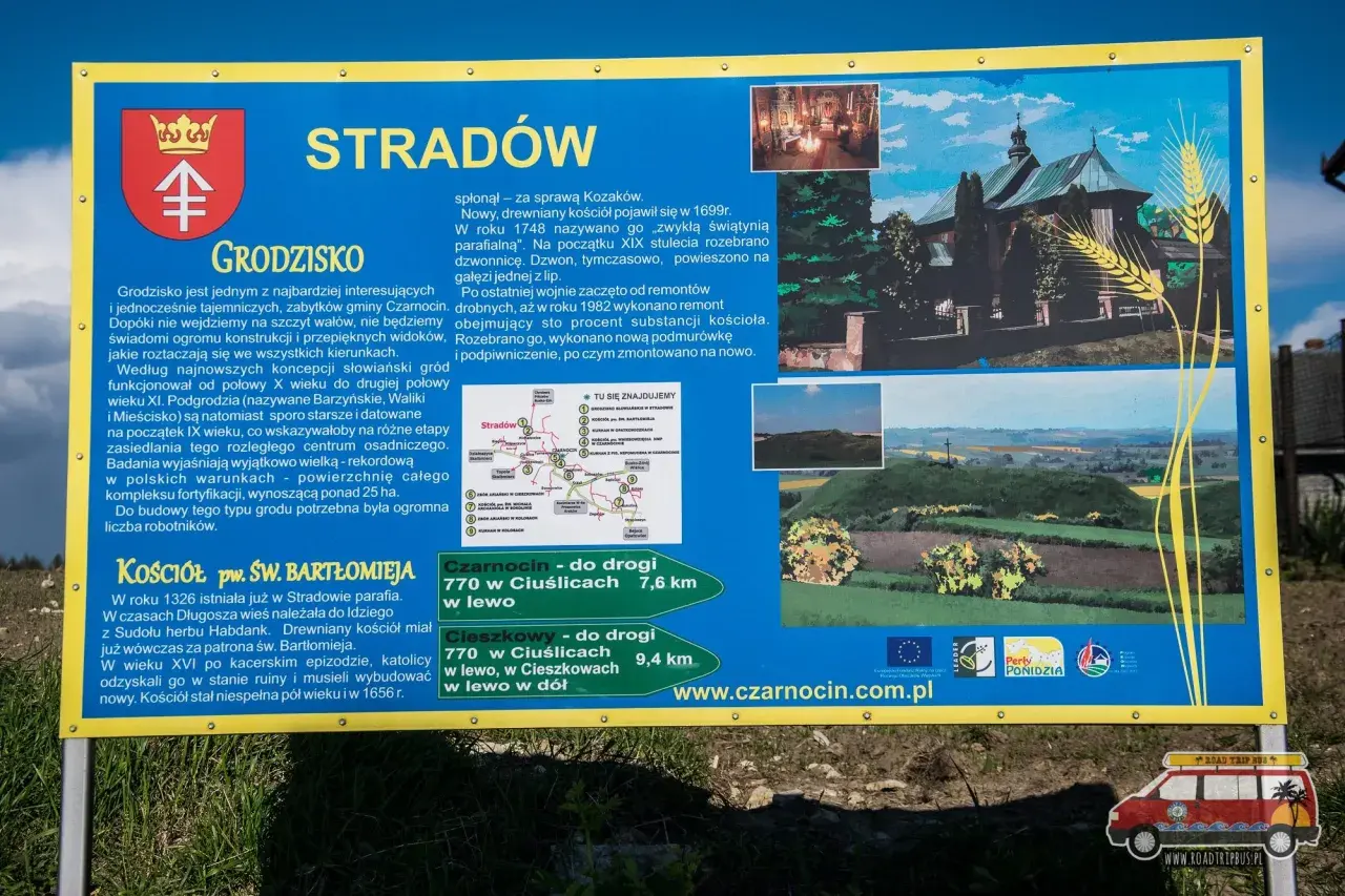 Tablica informacyjna o grodzisku Stradów, jego historii i kościele pw. św. Bartłomieja. Widok na krajobraz z wałami grodziska.