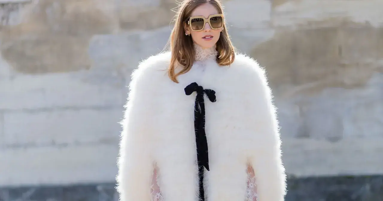 Estilo maximalismo: mujer con abrigo blanco de pelo, gafas grandes y lazo negro.