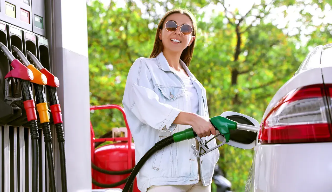 Uśmiechnięta kobieta tankuje auto. W tle zielone drzewa.