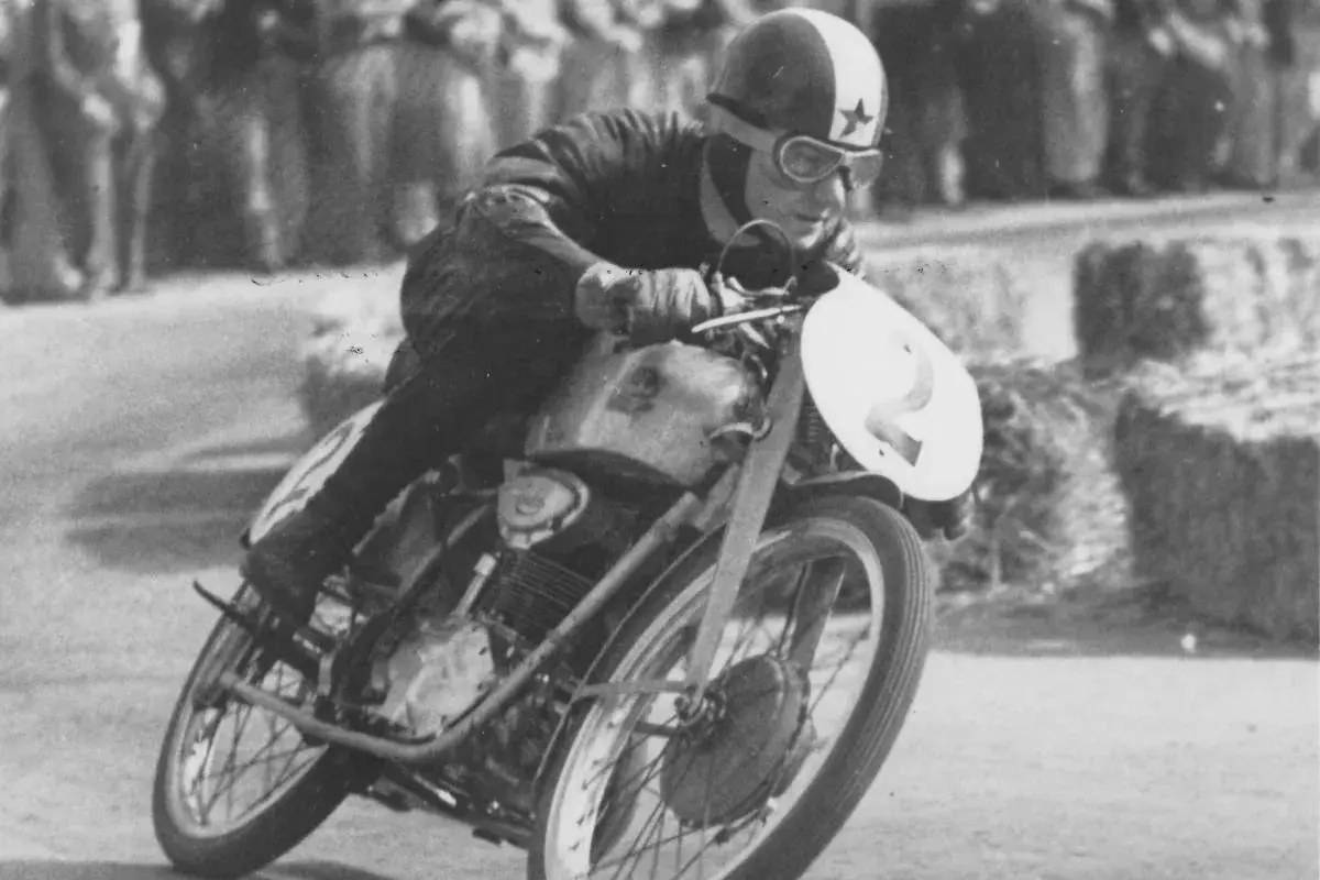 El piloto de carreras Carlo Ubbiali inclinado en su moto con el número 2, compitiendo con determinación.