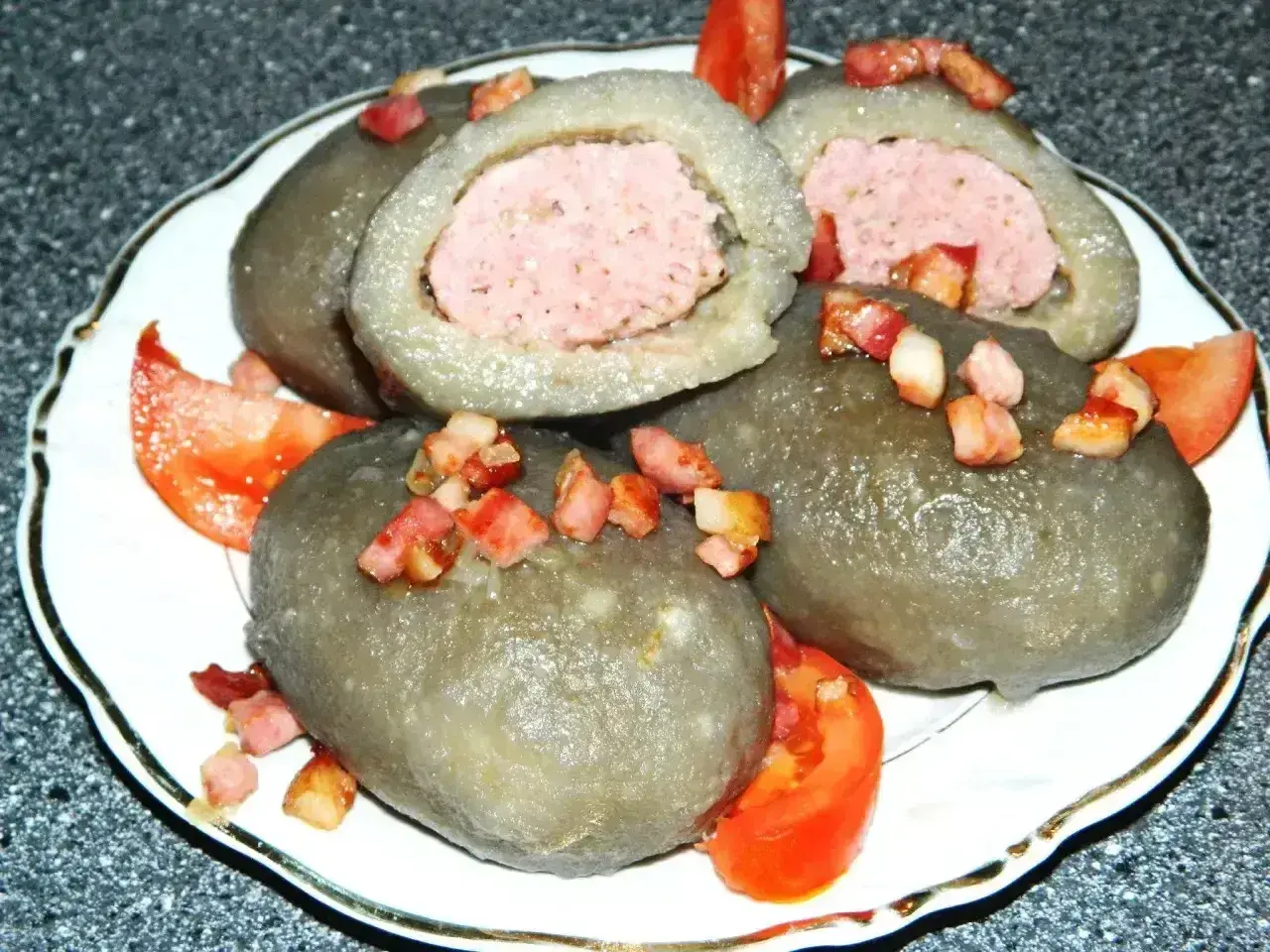 Cepelin z mięsem, polany skwarkami i podany z pomidorem. Wyglądają jak małe cepeliny na talerzu.