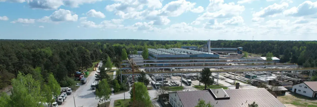 Fabryka domów Bogucin z lotu ptaka. Widok na hale produkcyjne, place składowe z elementami prefabrykowanymi i ciężarówki.